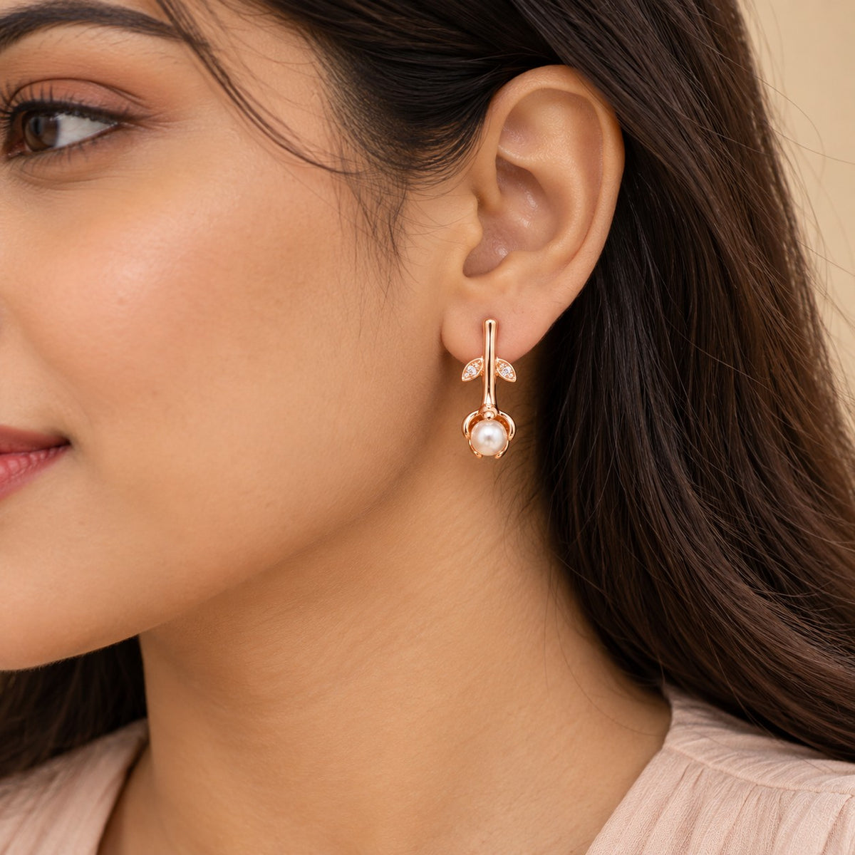Woman wearing a rose gold rosebud pearl drop earring, close-up of ear and jawline