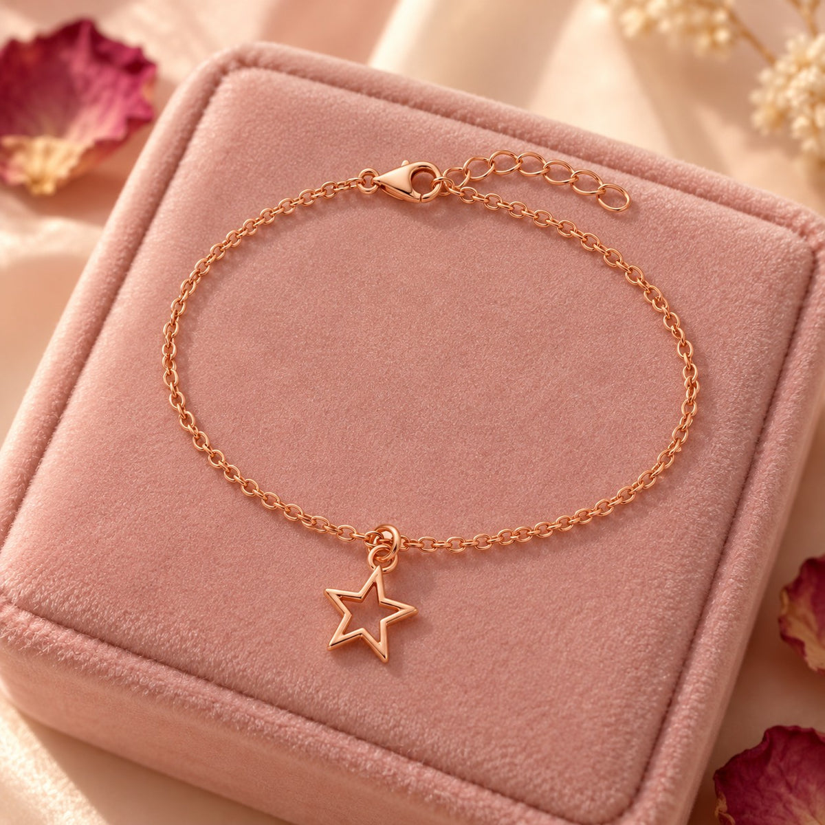Rose gold star charm bracelet styled on a blush velvet box with dried petals