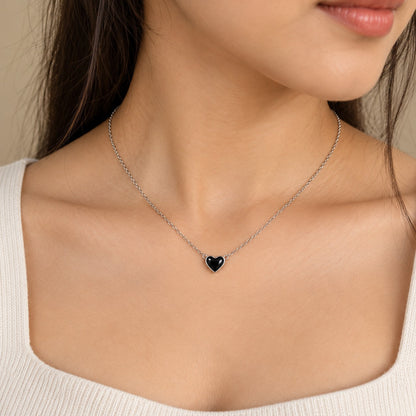 Woman wearing a silver chain necklace with a small black heart pendant