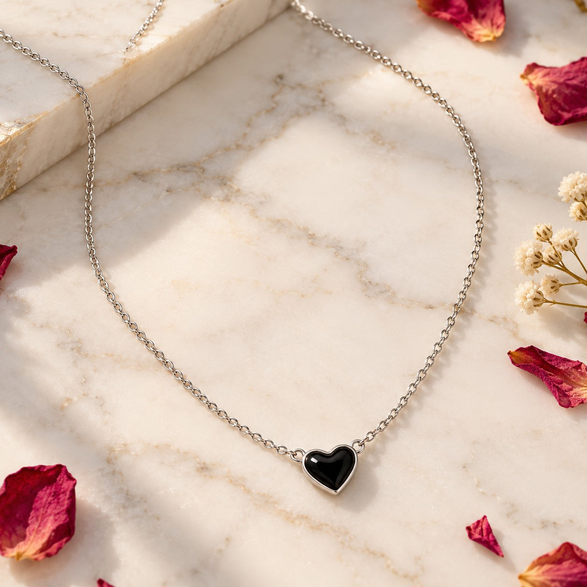 Silver black heart pendant chain necklace styled on white marble with petals