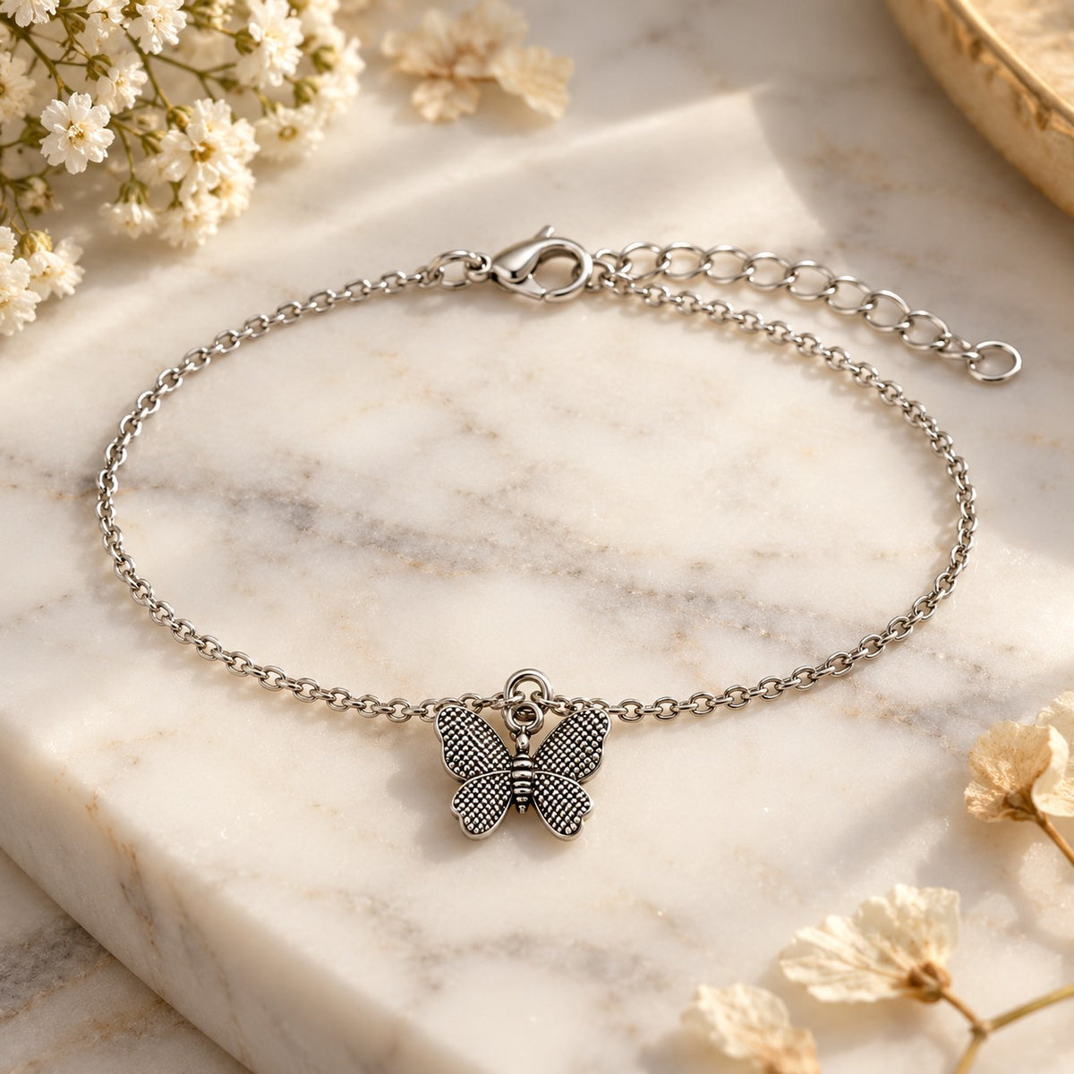 Silver butterfly charm bracelet styled on white marble with soft flowers