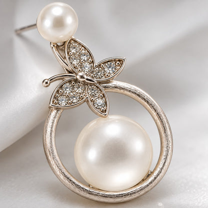 Macro view of the crystal butterfly and milky faux pearl on a silver circle drop earring