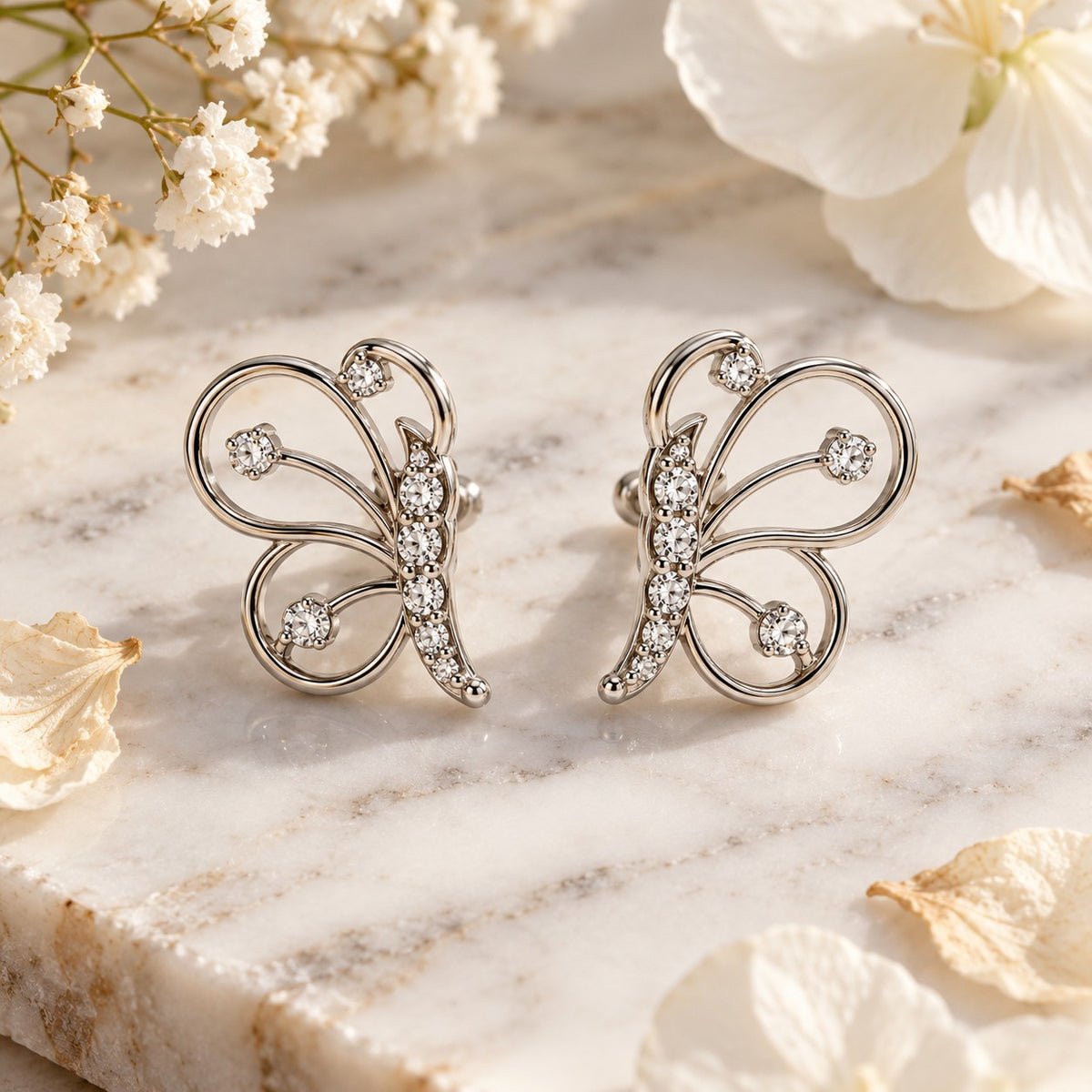 Silver butterfly stud earrings on white marble with soft dried flowers
