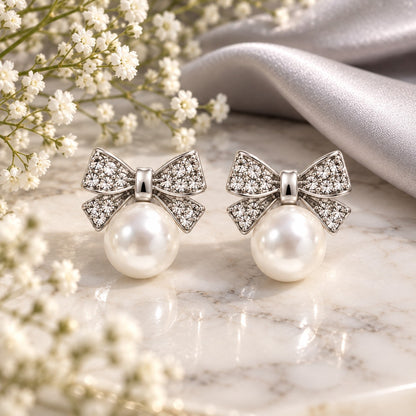 Silver crystal bow pearl stud earrings on white marble with baby's breath flowers