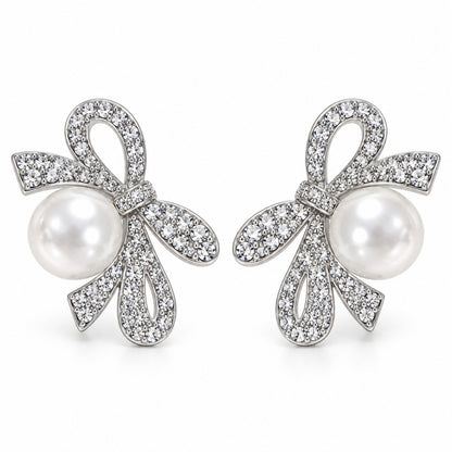 Silver crystal ribbon bow pearl drop earrings with large faux pearl on a white background