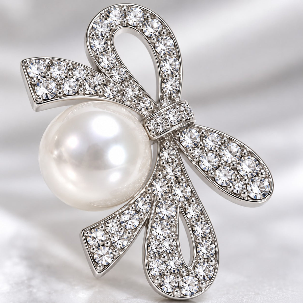 Macro view of the crystal-paved silver ribbon bow and faux pearl on a drop earring