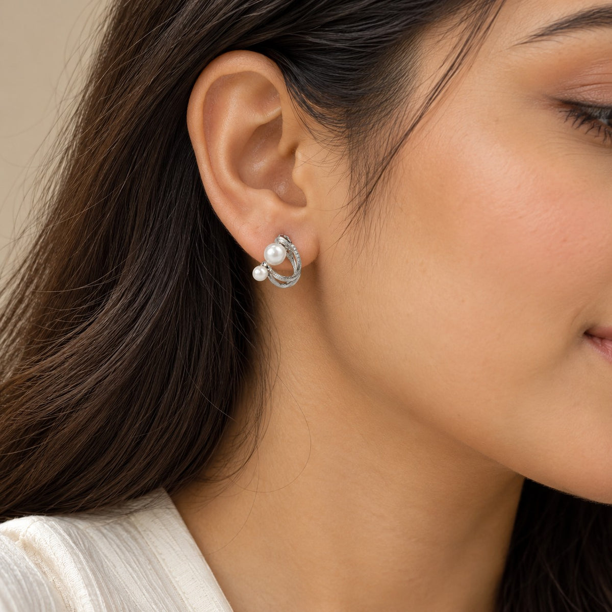 Woman wearing silver double pearl twisted hoop stud earrings, close-up of ear and jawline