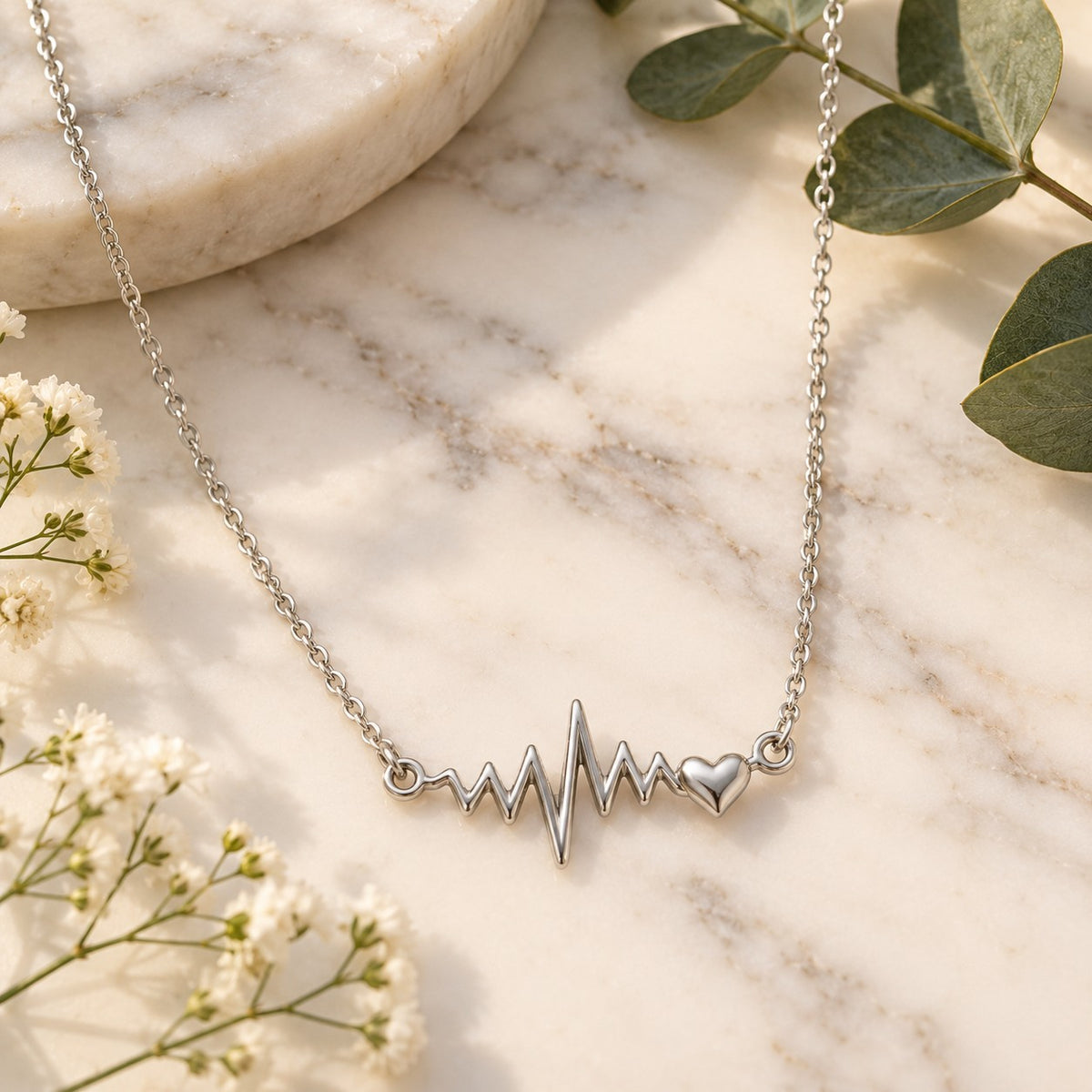 Silver heartbeat pendant chain necklace styled on white marble with flowers