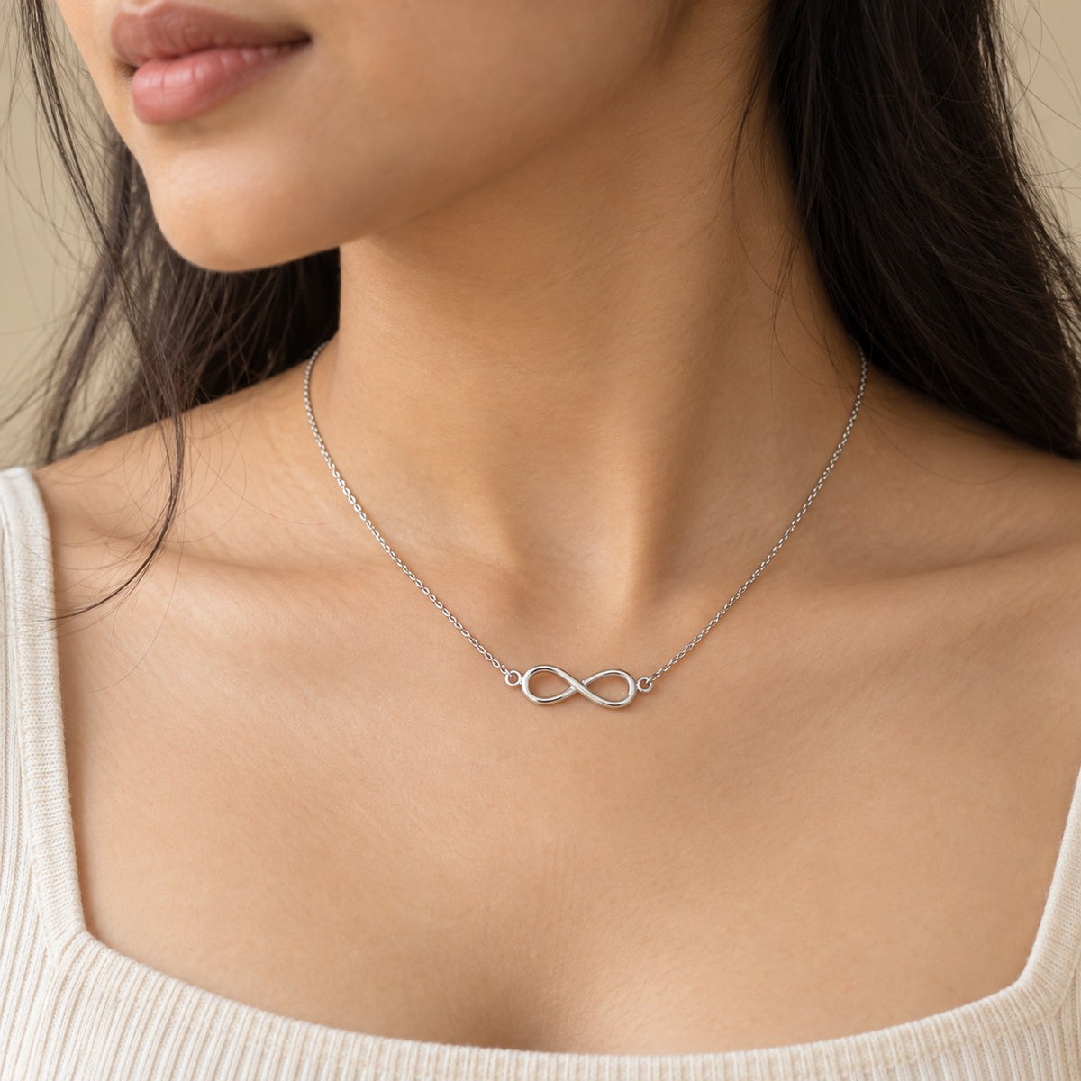 Woman wearing silver infinity pendant chain necklace, close-up of collarbone and neckline