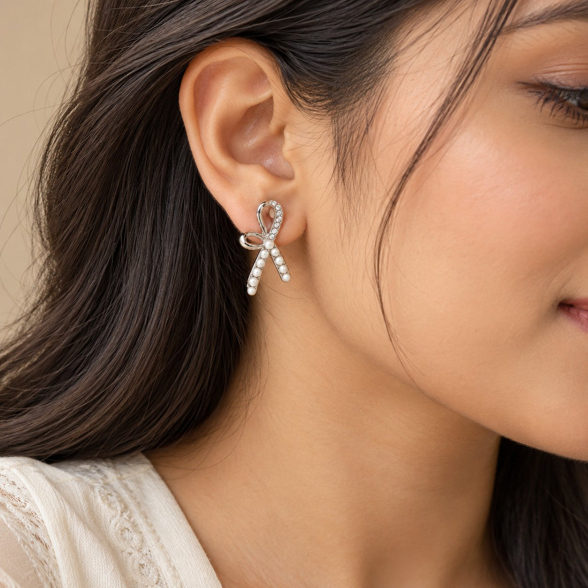 Woman wearing a silver pearl ribbon bow stud earring, close-up of ear and jawline