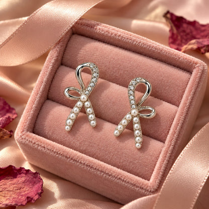Silver pearl ribbon bow stud earrings on a blush-pink velvet box with dried petals