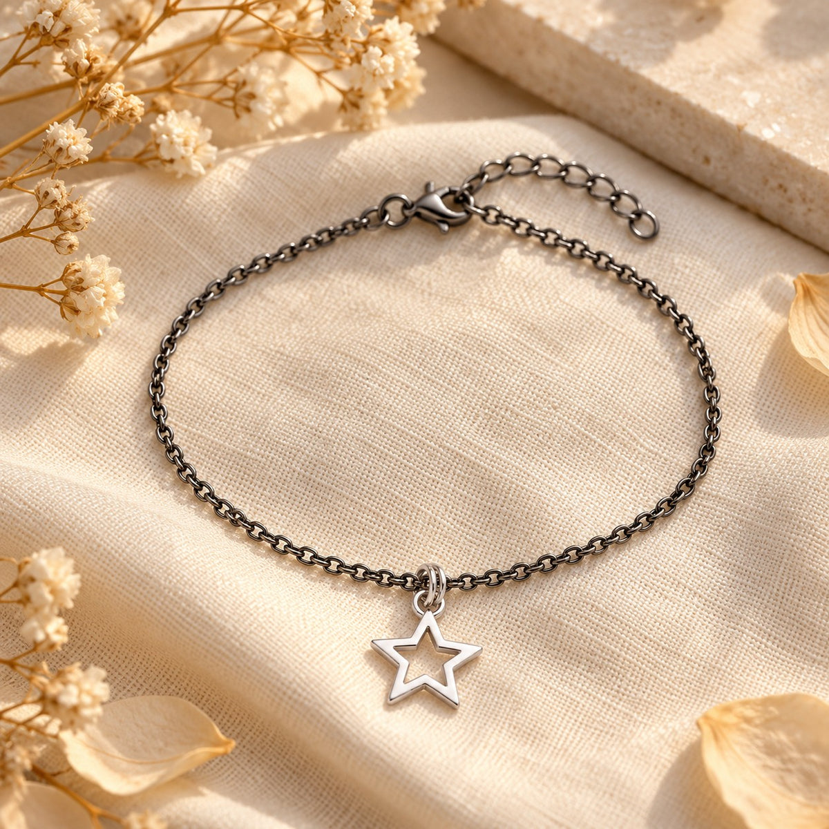 Silver star charm bracelet styled on linen with dried flowers in warm light