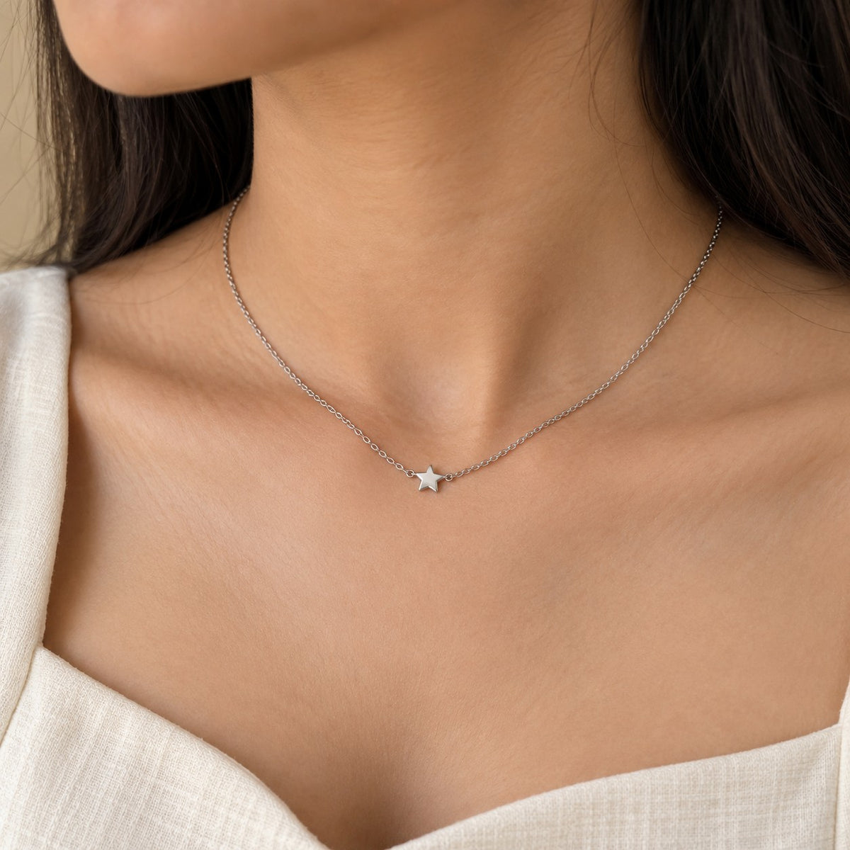 Woman wearing a dainty silver chain necklace with a tiny star pendant