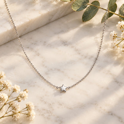 Silver star pendant chain necklace styled on white marble with soft flowers