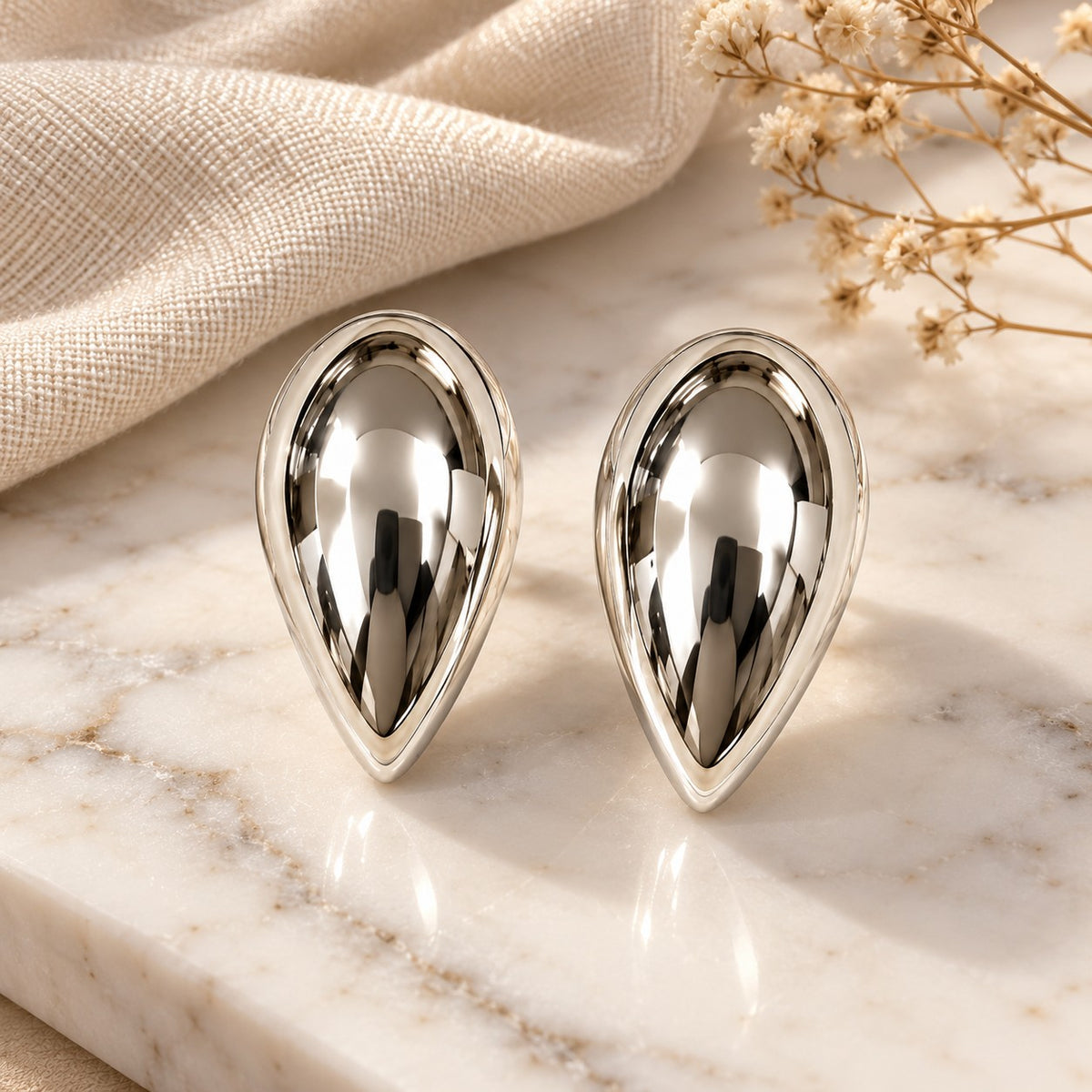 Silver teardrop dome stud earrings on white marble with soft linen and dried flowers